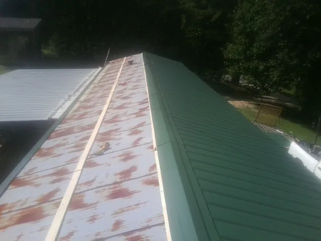 Old rusted panels beside newly installed green metal roofing — Wind Damage Roof Repair by Roofing Brothers in Malta